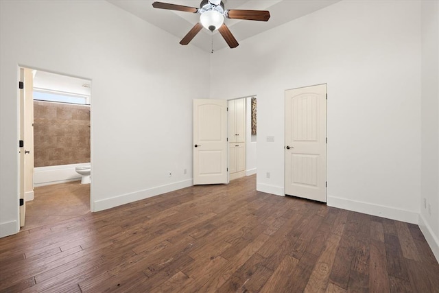 unfurnished bedroom with baseboards, ensuite bathroom, a towering ceiling, and dark wood-type flooring