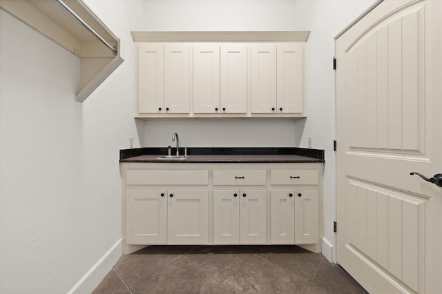 clothes washing area featuring dark tile patterned flooring, baseboards, indoor wet bar, and a sink