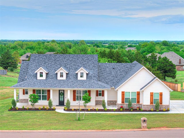 new england style home featuring covered porch, fence, a front yard, and roof with shingles