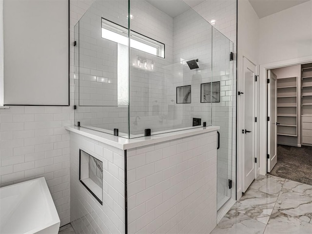bathroom with tile walls, a tub, a stall shower, marble finish floor, and a spacious closet