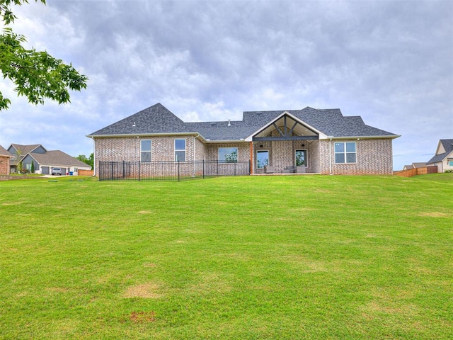 view of front facade featuring a front yard, fence, a shingled roof, and brick siding