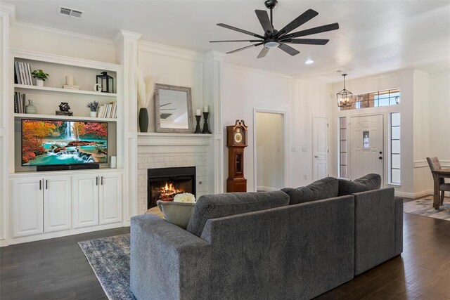 2201 Pine View Ter, Edmond, OK 73003 - living room featuring dark wood finished floors, a ceiling fan, crown molding, a brick fireplace, and a chandelier