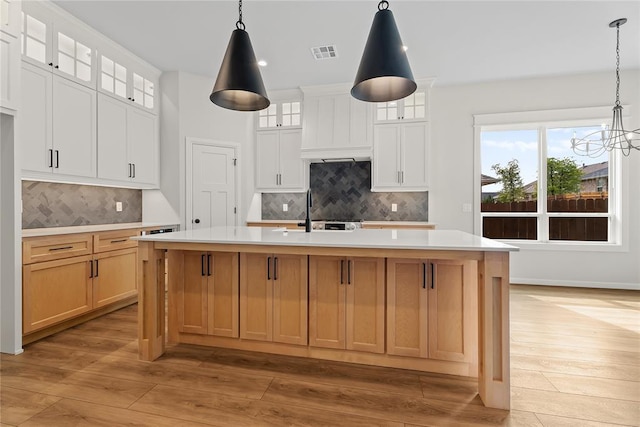 kitchen featuring visible vents, a sink, light countertops, an island with sink, and light wood-style floors