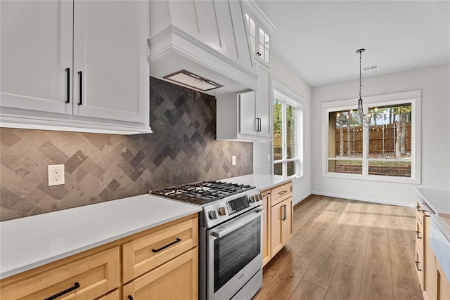 kitchen featuring a notable chandelier, light wood-style flooring, light countertops, premium range hood, and stainless steel range with gas cooktop