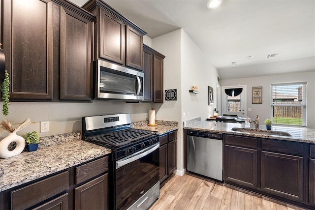 1105 NW 3rd St, Newcastle, OK 73065 - kitchen featuring light wood-style flooring, a sink, dark brown cabinetry, appliances with stainless steel finishes, and light stone counters