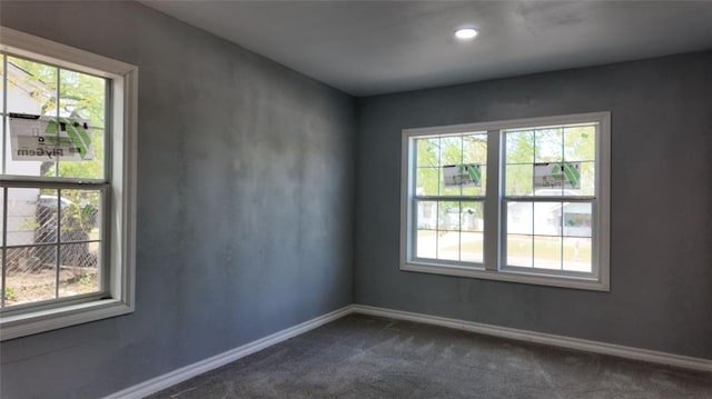 empty room with dark carpet, a wealth of natural light, and baseboards