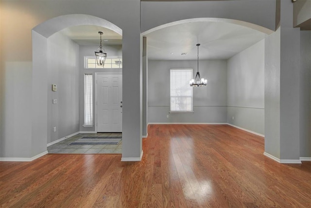 foyer entrance featuring arched walkways, a notable chandelier, wood finished floors, and baseboards