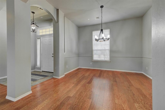 unfurnished dining area with wood finished floors, a chandelier, arched walkways, baseboards, and visible vents