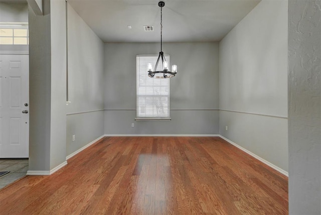 interior space with a chandelier, wood finished floors, visible vents, and baseboards