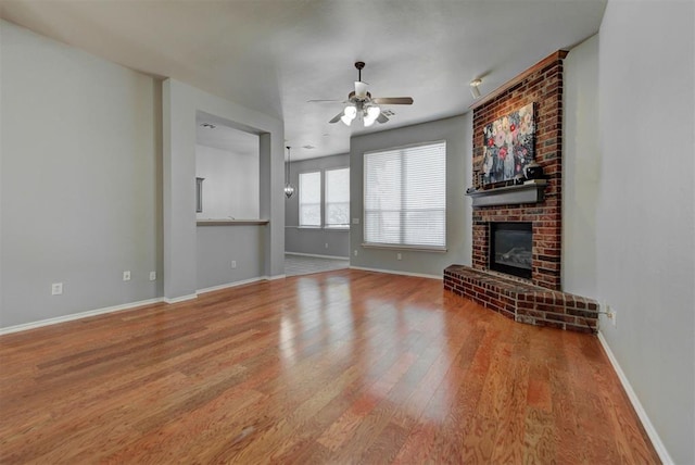 unfurnished living room featuring ceiling fan, baseboards, a brick fireplace, and wood finished floors
