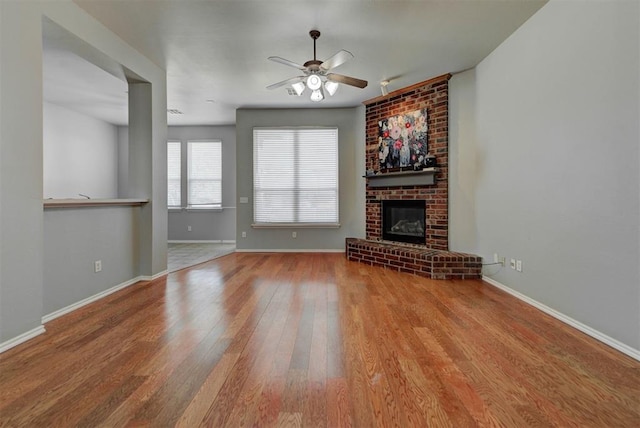 unfurnished living room featuring baseboards, a brick fireplace, wood finished floors, and ceiling fan