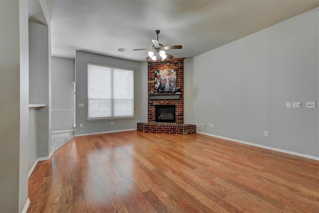 unfurnished living room with a ceiling fan, wood finished floors, baseboards, a brick fireplace, and visible vents