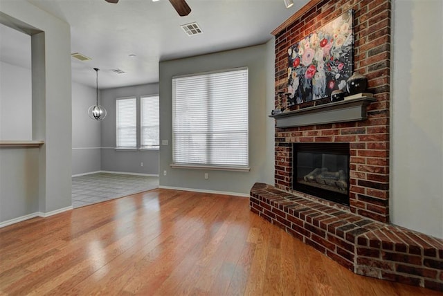 unfurnished living room featuring wood finished floors, visible vents, baseboards, a fireplace, and ceiling fan