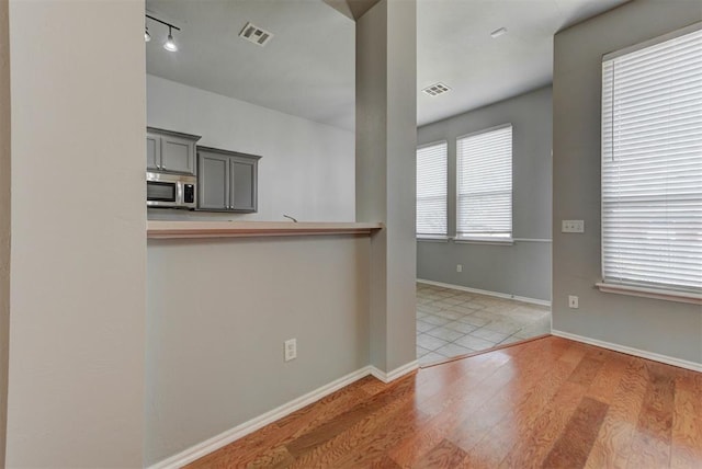 kitchen with stainless steel microwave, wood finished floors, visible vents, and baseboards