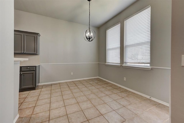 unfurnished dining area with baseboards, a notable chandelier, and light tile patterned floors