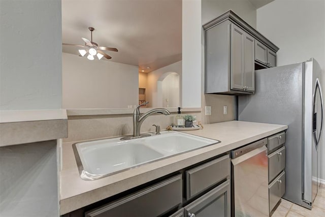 kitchen featuring a ceiling fan, stainless steel dishwasher, a sink, arched walkways, and gray cabinetry