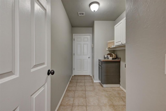 hall featuring baseboards, visible vents, and light tile patterned floors