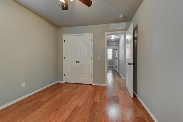 unfurnished bedroom featuring wood finished floors, visible vents, a closet, baseboards, and ceiling fan
