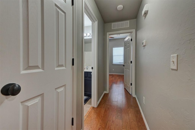 hall with light wood-style floors, visible vents, and baseboards