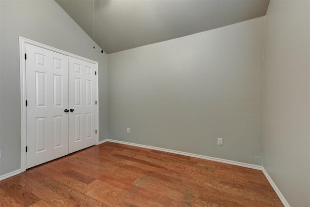 unfurnished bedroom with baseboards, vaulted ceiling, wood finished floors, and a closet