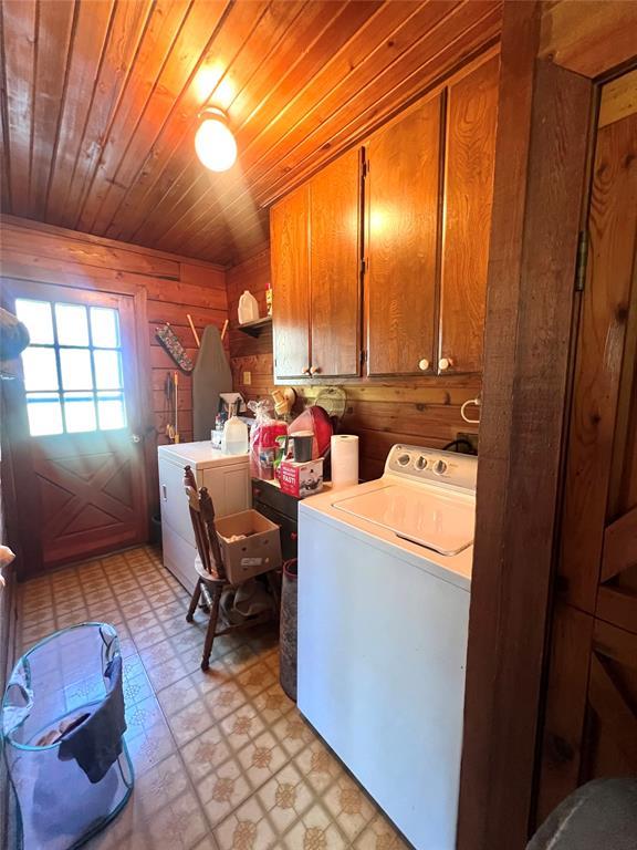 laundry area featuring wood walls, light floors, washer and clothes dryer, wooden ceiling, and cabinet space