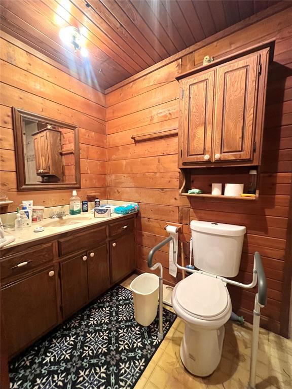 bathroom with vanity, wooden walls, wooden ceiling, toilet, and tile patterned flooring