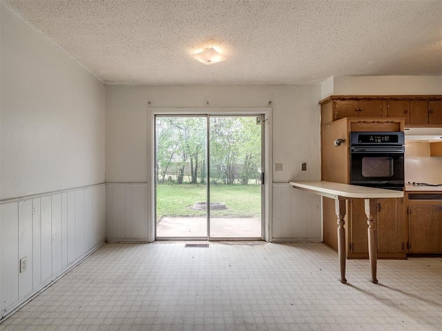 320 Willow Pl, Yukon, OK 73099 - kitchen with a textured ceiling, wainscoting, light floors, exhaust hood, and black oven