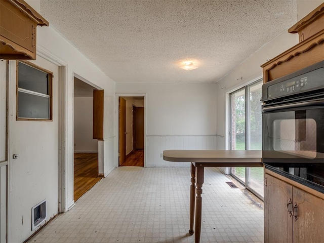 320 Willow Pl, Yukon, OK 73099 - kitchen with a textured ceiling, wainscoting, oven, light floors, and visible vents