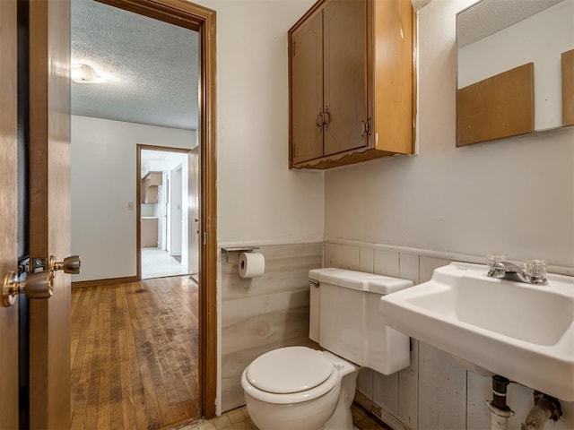 320 Willow Pl, Yukon, OK 73099 - half bath featuring wood finished floors, a textured ceiling, a sink, wainscoting, and toilet