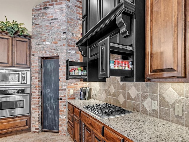 13401 Grapevine Trl, Oklahoma City, OK 73170 - kitchen featuring stainless steel appliances, tasteful backsplash, light tile patterned floors, light stone countertops, and brown cabinets