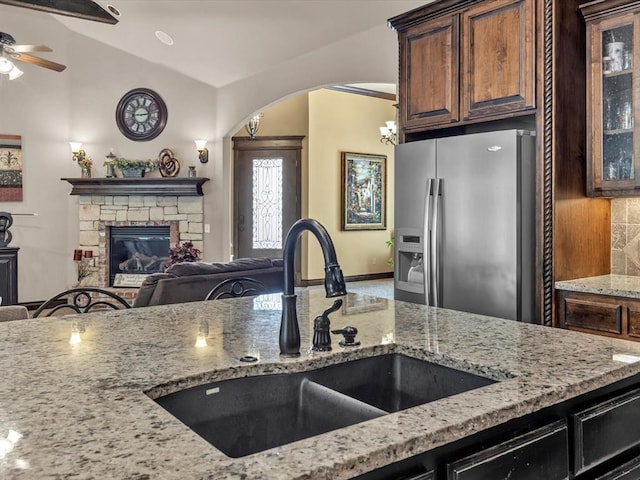 13401 Grapevine Trl, Oklahoma City, OK 73170 - kitchen with stainless steel fridge, a sink, arched walkways, light stone counters, and a fireplace