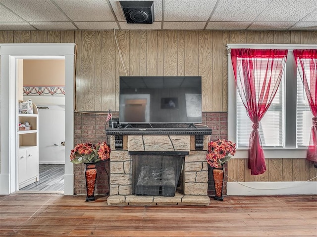 living room with a stone fireplace, wood finished floors, and a drop ceiling