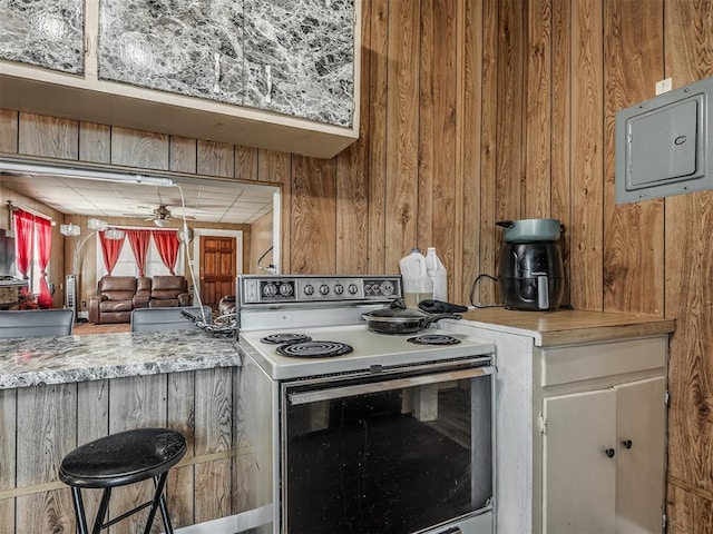 kitchen featuring electric range oven, a ceiling fan, wooden walls, and light countertops