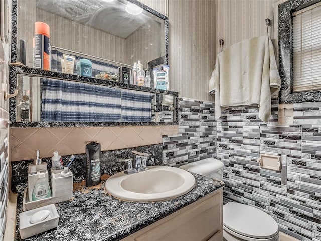 half bath featuring wallpapered walls, decorative backsplash, vanity, tile walls, and toilet