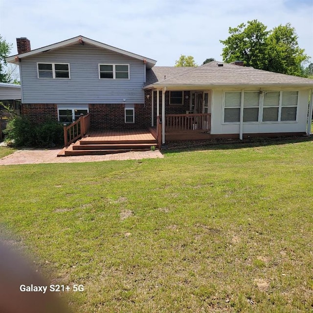 rear view of property with a chimney, brick siding, a wooden deck, and a yard