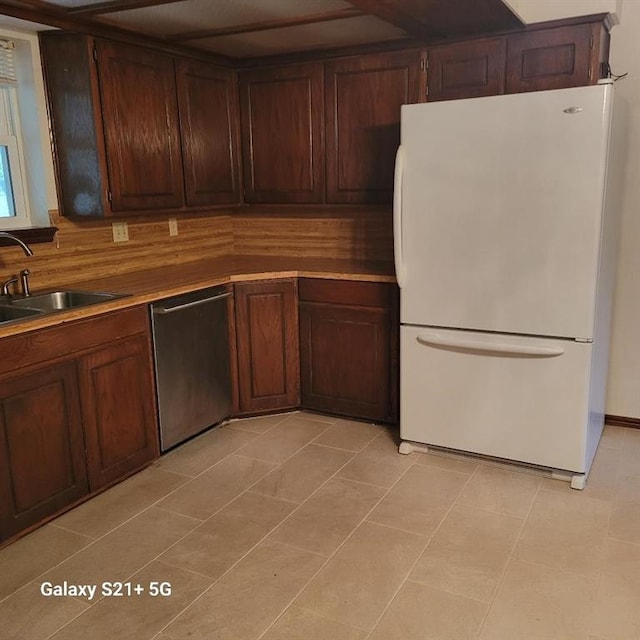 kitchen featuring a sink, light tile patterned floors, tasteful backsplash, stainless steel dishwasher, and freestanding refrigerator