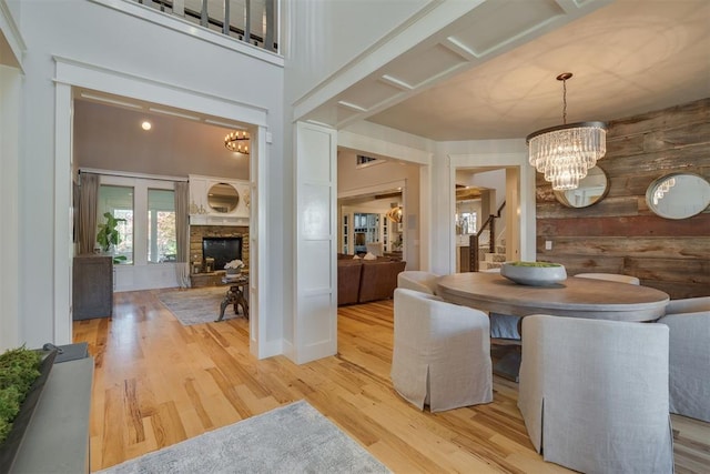 dining room with a stone fireplace, wood finished floors, a chandelier, wooden walls, and stairs