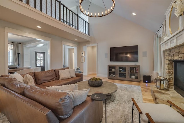 living room with high vaulted ceiling, a notable chandelier, a stone fireplace, and light wood-style flooring