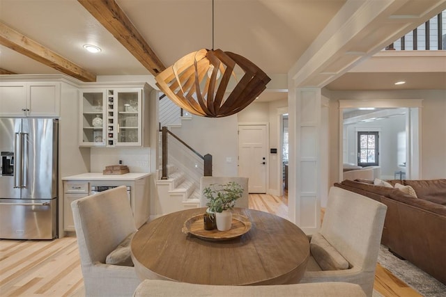 dining space with stairway, a dry bar, light wood finished floors, and beam ceiling
