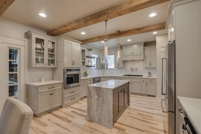 kitchen featuring appliances with stainless steel finishes, light wood-style flooring, tasteful backsplash, a kitchen island, and glass insert cabinets