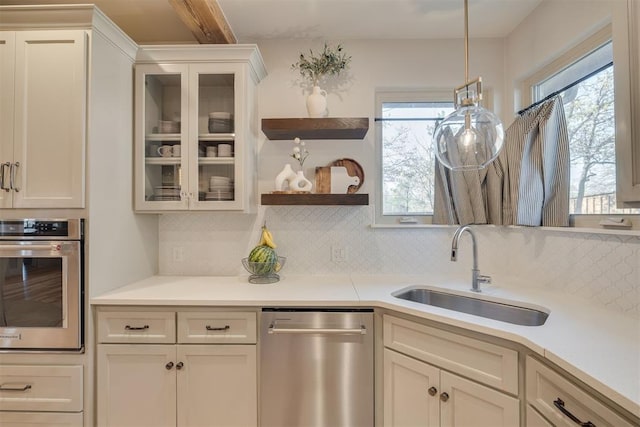 kitchen featuring a sink, light countertops, stainless steel appliances, decorative backsplash, and glass insert cabinets