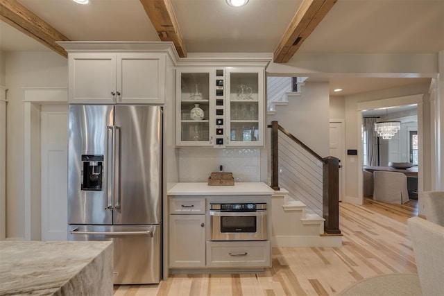 kitchen featuring beam ceiling, glass insert cabinets, light wood-style floors, tasteful backsplash, and stainless steel appliances