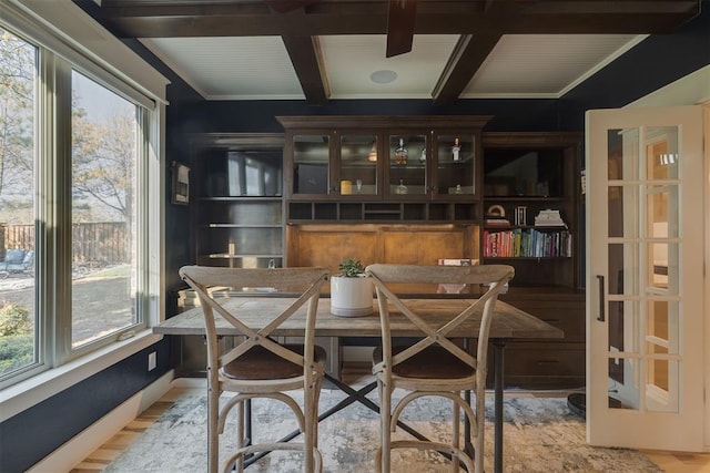 dining area with light wood-style floors, coffered ceiling, a wealth of natural light, and beamed ceiling