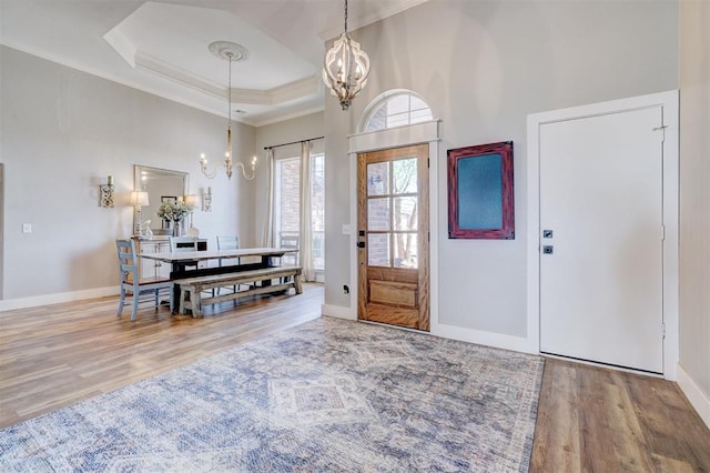 entryway featuring crown molding, a chandelier, a raised ceiling, baseboards, and wood finished floors
