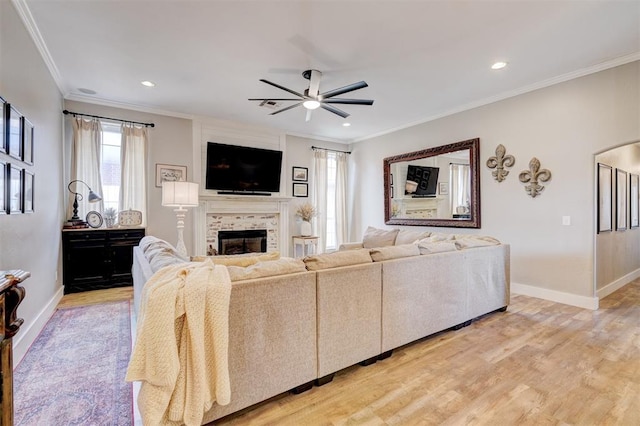 living room with ceiling fan, a tiled fireplace, ornamental molding, and baseboards