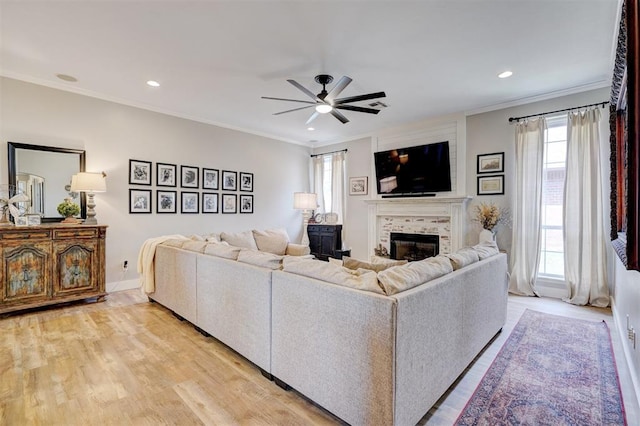 living area with ornamental molding, ceiling fan, a tile fireplace, and light wood finished floors
