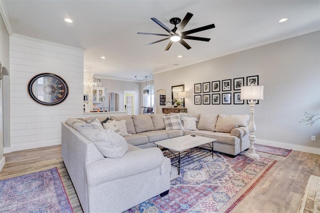 living room with light wood-type flooring, recessed lighting, ornamental molding, and ceiling fan with notable chandelier