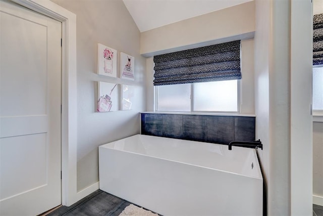 full bathroom featuring a freestanding bath, vaulted ceiling, and baseboards