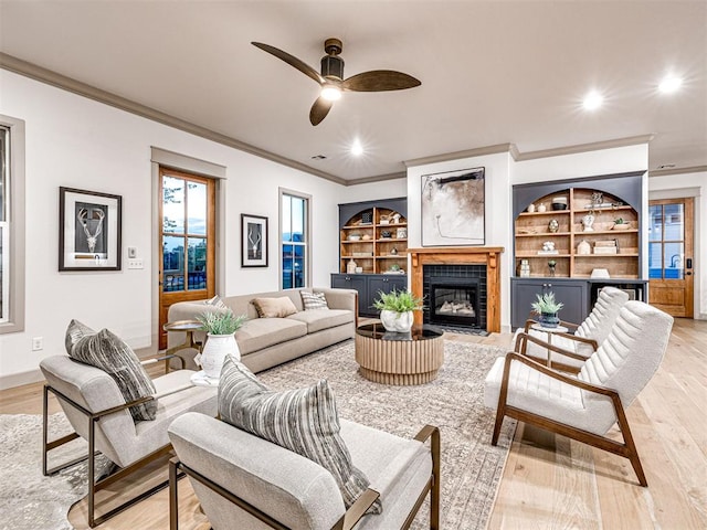 18443 Boardwalk Xing, Norman, OK 73072 - living area featuring light wood-style flooring, a tiled fireplace, ceiling fan, built in features, and crown molding