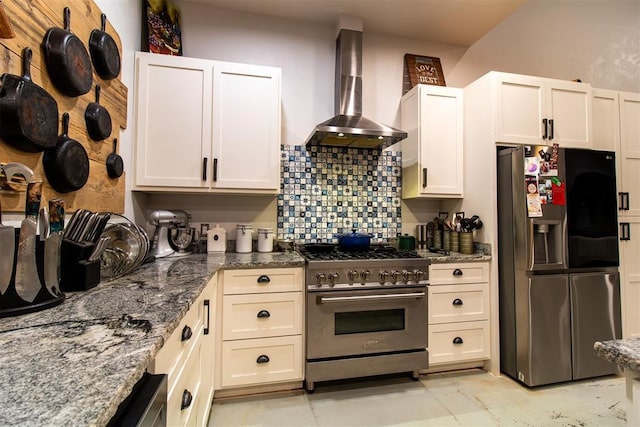 kitchen with backsplash, white cabinetry, dark stone countertops, stainless steel appliances, and wall chimney exhaust hood